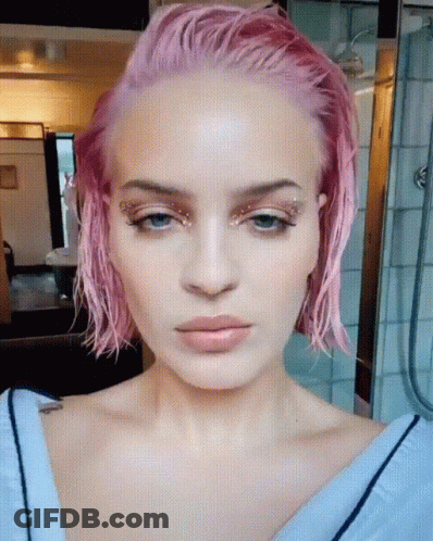 A Close Up Of A Woman 'S Face With Pink Hair And Blue Eyes GIF