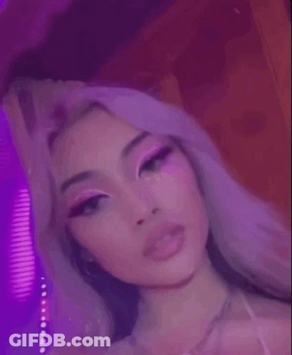 A Close Up Of A Woman 'S Face With Pink Makeup And Purple Lights Behind Her . GIF