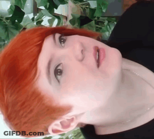 A Close Up Of A Woman 'S Face With Red Hair And Black Shirt GIF