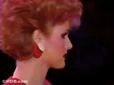 A Close Up Of A Woman 'S Face With Red Hair And Red Earrings . GIF