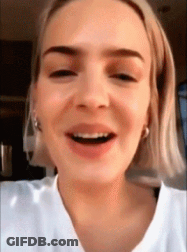 A Close Up Of A Woman 'S Face With Short Blonde Hair And A White Shirt Smiling . GIF