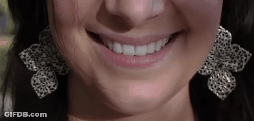 A Close Up Of A Woman 'S Mouth Wearing Earrings And Smiling GIF