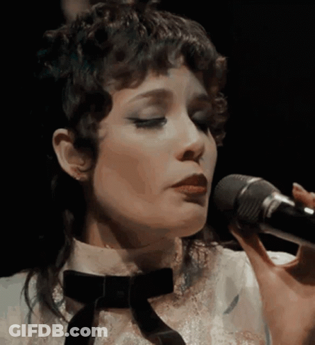 A Close Up Of A Woman Singing Into A Microphone With Her Eyes Closed GIF