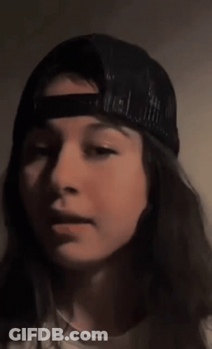 A Close Up Of A Woman Wearing A Baseball Cap Covering Her Mouth With Her Hand . GIF