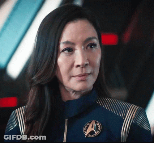 A Close Up Of A Woman Wearing A Blue Jacket With A Star Trek Emblem On It . GIF