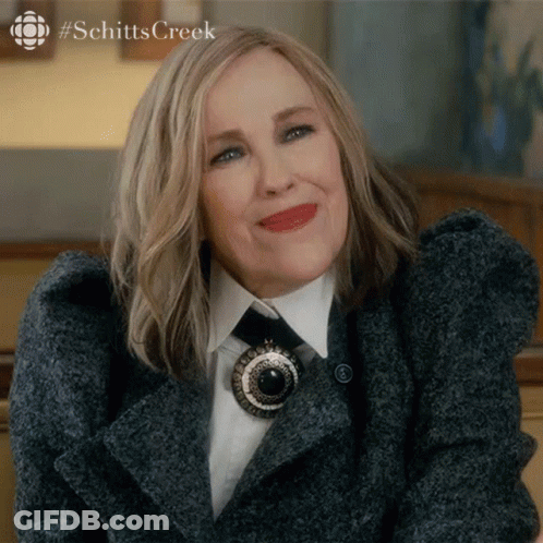 A Close Up Of A Woman Wearing A Coat And Tie With The Word Schitts Creek In The Corner GIF