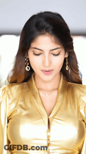 A Close Up Of A Woman Wearing A Gold Shirt And Earrings GIF