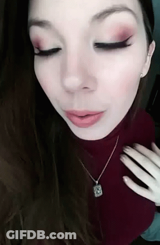 A Close Up Of A Woman Wearing A Necklace And A Red Turtleneck Sweater . GIF