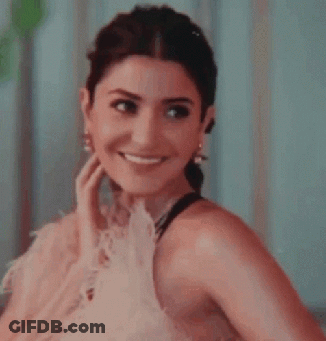 A Close Up Of A Woman Wearing A Pink Dress And Earrings Smiling . GIF