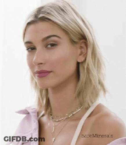 A Close Up Of A Woman Wearing A Purple Shirt And A Necklace With Bareminerals Written On Her Arm GIF