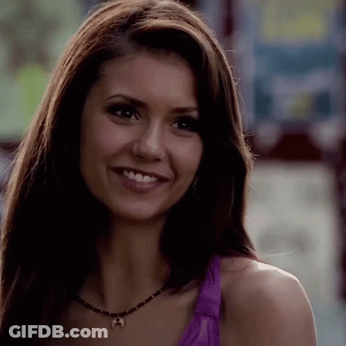 A Close Up Of A Woman Wearing A Purple Tank Top And A Necklace Smiling . GIF