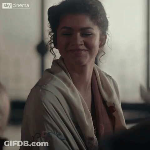 A Close Up Of A Woman Wearing A Scarf Around Her Neck And Smiling . GIF