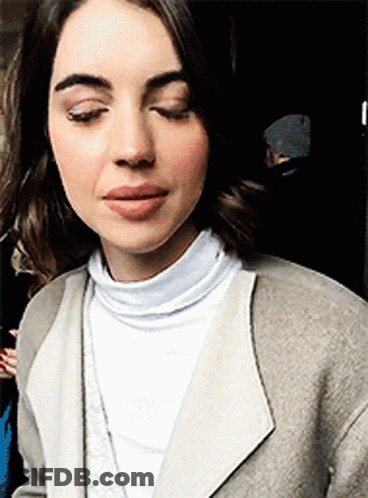 A Close Up Of A Woman Wearing A White Turtleneck And A Gray Coat . GIF