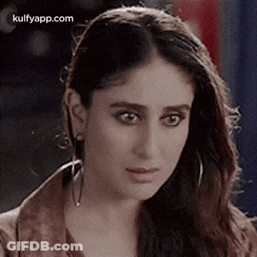 A Close Up Of A Woman Wearing Earrings And A Brown Jacket Looking At The Camera . GIF
