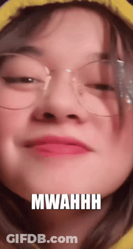 A Close Up Of A Woman Wearing Glasses And A Yellow Hoodie With The Words Mwahhh Written On Her Face . GIF