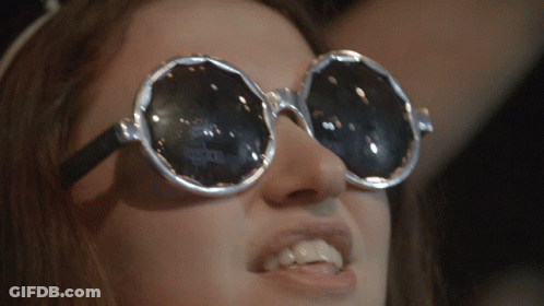 A Close Up Of A Woman Wearing Sunglasses With A Reflection Of A Person 'S Face In Them GIF
