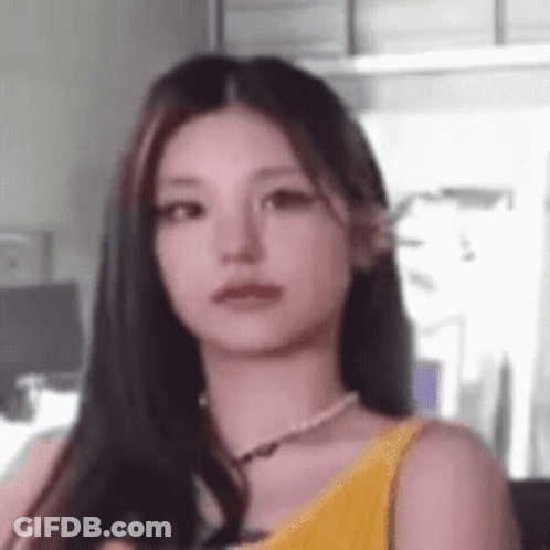 A Close Up Of A Woman With Long Hair Wearing A Yellow Tank Top And A Pearl Necklace . GIF