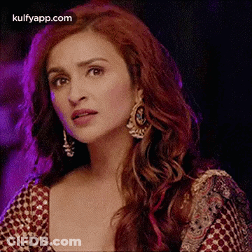 A Close Up Of A Woman With Red Hair Wearing Earrings And A Red Top . GIF