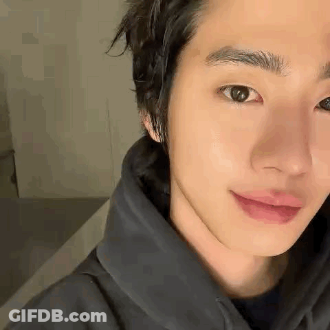 A Close Up Of A Young Man 'S Face Wearing A Black Hoodie And Smiling . GIF