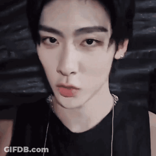A Close Up Of A Young Man 'S Face Wearing A Black Tank Top And Necklace . GIF
