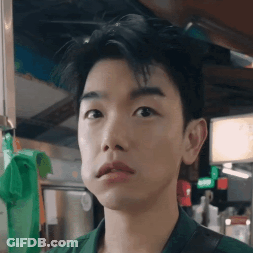A Close Up Of A Young Man 'S Face With A Green Bag Hanging On The Wall Behind Him GIF