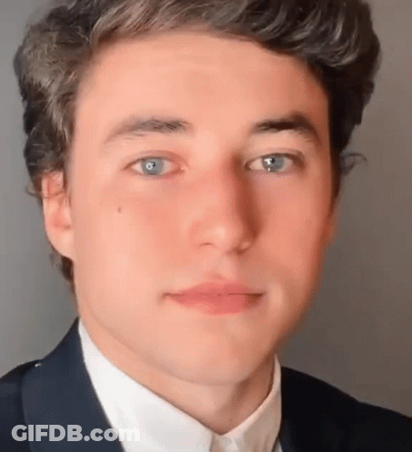 A Close Up Of A Young Man 'S Face With Blue Eyes Wearing A Suit And White Shirt . GIF