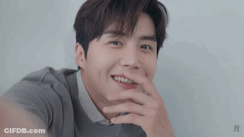 A Close Up Of A Young Man Smiling With His Hand On His Mouth . GIF