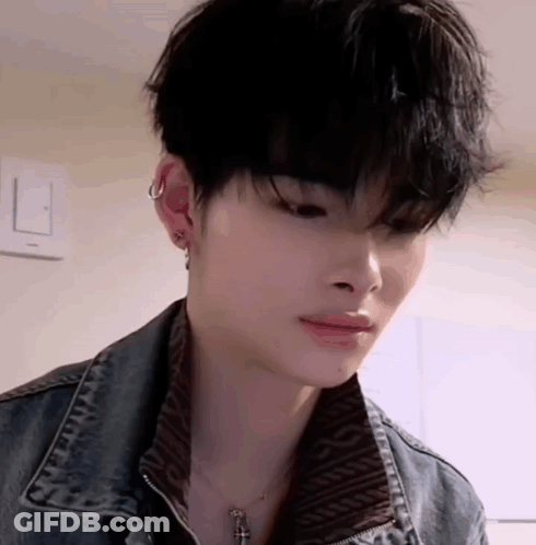 A Close Up Of A Young Man Wearing A Denim Jacket And A Necklace With A Cross . GIF