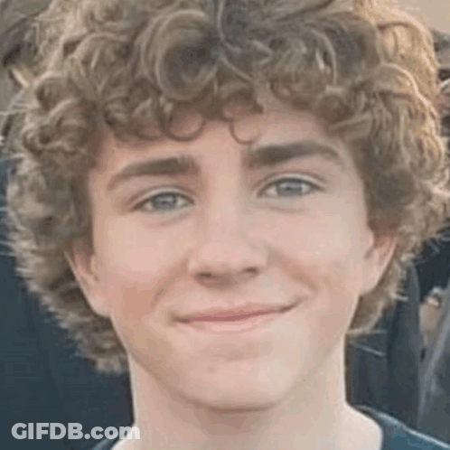 A Close Up Of A Young Man With Curly Hair Smiling For The Camera . GIF