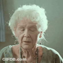 A Close Up Of An Elderly Woman With Her Eyes Closed And A Necklace Around Her Neck GIF