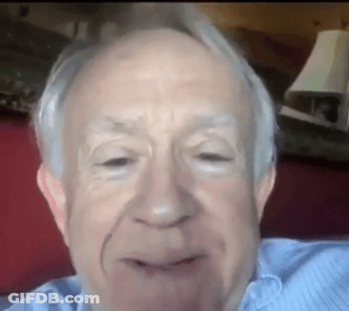 A Close Up Of An Older Man 'S Face With A Lamp Behind Him GIF
