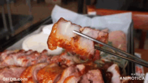 A Close Up Of Chopsticks Holding A Piece Of Meat Over A Plate Of Meat GIF