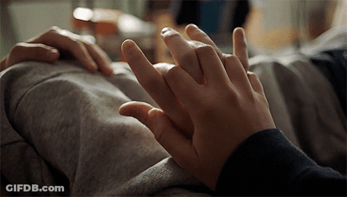 A Close Up Of Two People Holding Hands On A Bed GIF
