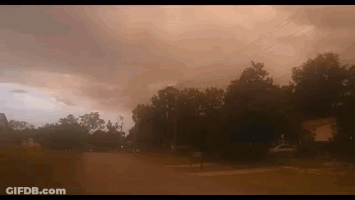 A Cloudy Sky With A Few Trees In The Foreground And A Few Houses In The Background GIF