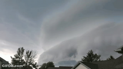 A Cloudy Sky With A House In The Foreground And Trees In The Background GIF