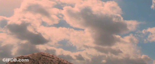 A Cloudy Sky With A Tower On Top Of A Rock GIF