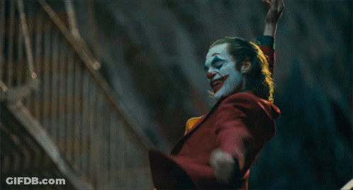 A Clown In A Red Suit And Yellow Vest Is Waving GIF