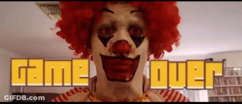 A Clown In A Red Wig Is Standing In Front Of A Game Over Sign GIF