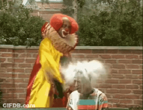 A Clown In A Yellow And Red Costume Is Standing Next To A Woman . GIF