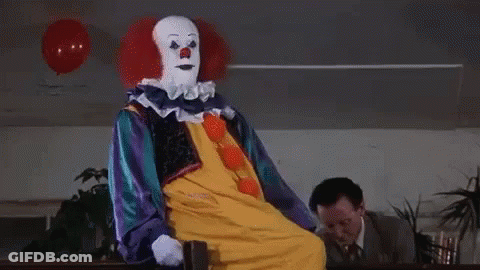 A Clown Is Sitting In A Chair In Front Of A Man In A Suit . GIF