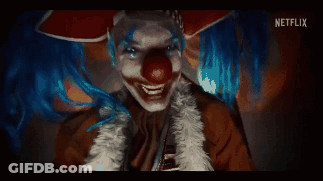 A Clown With Blue Hair And A Red Nose Is Smiling And Looking At The Camera . GIF