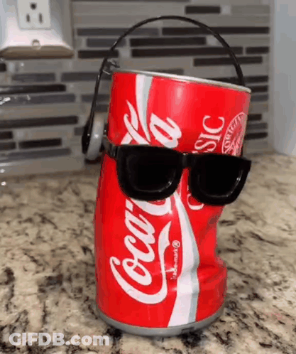 A Coca Cola Can With Sunglasses And Headphones On It Is Sitting On A Counter . GIF