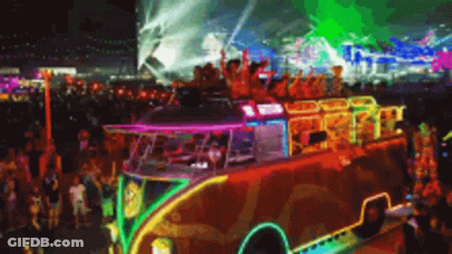 A Colorful Bus Is Driving Through A Crowd Of People At A Festival GIF