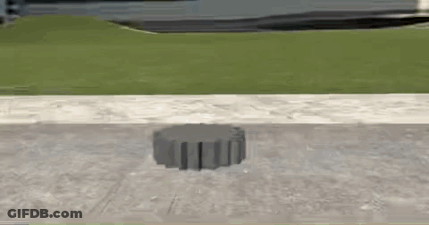 A Concrete Block Is Sitting On The Sidewalk Next To A Grassy Hill . GIF