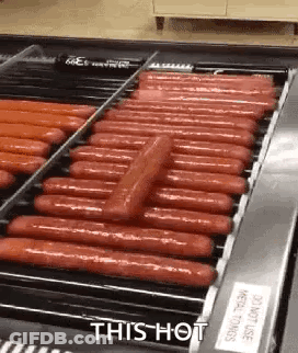 A Conveyor Belt Filled With Hot Dogs Is Being Cooked . GIF