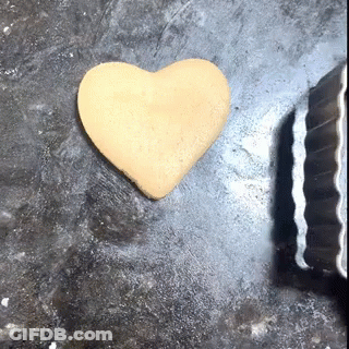 A Cookie In The Shape Of A Heart Is On A Table Next To A Cookie Cutter GIF