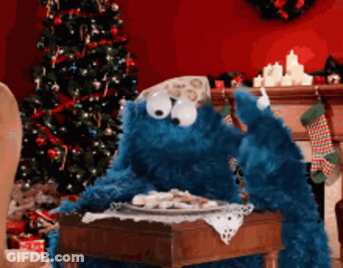 A Cookie Monster Sits At A Table With A Plate Of Cookies GIF