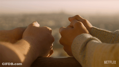A Couple Holding Hands With A Netflix Logo Behind Them GIF