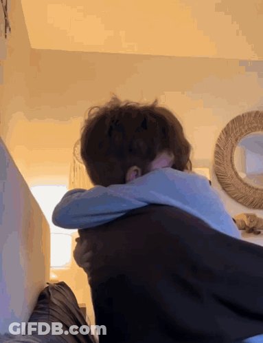 A Couple Hugging Each Other In A Room With A Mirror In The Background GIF