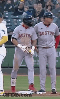A Couple Of Baseball Players Are Standing On A Field . One Of The Players Is Wearing A Boston Jersey . GIF
